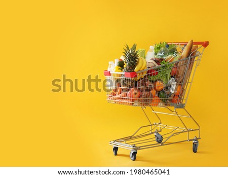 Shopping cart full of groceries on yellow background. Space for text