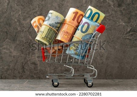 Shopping cart full of roll euro banknotes.Shopping costs money.