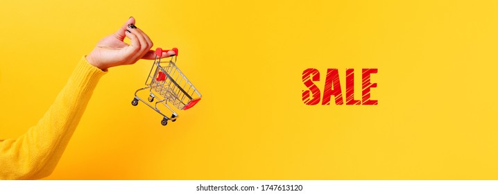 Shopping Cart In Hand With Inscription Sale Over Yellow Background,  Panoramic Image