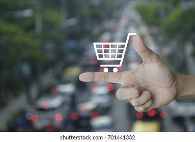 Shopping cart icon on finger over blur of rush hour with cars and road, Shop online concept