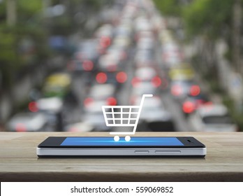 Shopping cart Icon on modern smart phone screen on wooden table over blur of rush hour with cars and road, Shop online concept