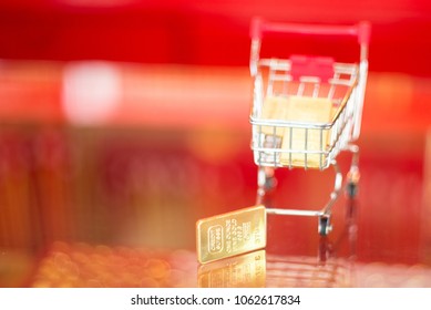 Shopping Cart With Mini Gold Bar, Red Background Blurred Copy Space