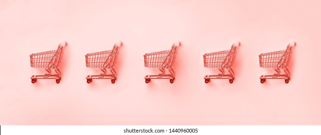 Shopping cart on trendy coral color background. Minimalism style. Creative design. Shop trolley at supermarket. Sale, discount, shopaholism concept. Consumer society trend.