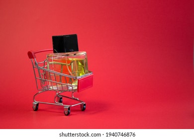 Shopping cart with perfume on red background, the concept of beauty, accessories with empty space