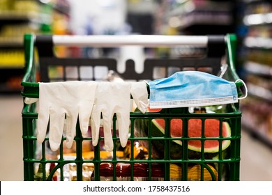 Shopping Cart With Protective Gloves And Mask Resting On The Handlebar, Filled With Food, No Person, Defocused Background.