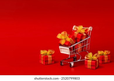 A shopping cart with red gifts with gold bows on a red background. Holidays, gifts, shopping copy space banner - Powered by Shutterstock