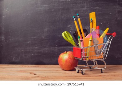 Shopping Cart With School Supplies Over Chalkboard Background