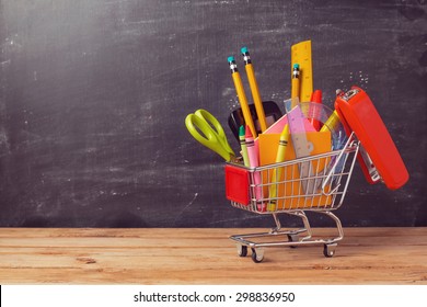 Shopping Cart With School Supplies Over Chalkboard Background. Back To School Sale Concept