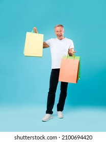 Shopping Concept. Excited Mature Man Holding Showing Paper Shopper Bags With Copy Space Mockup For Design Template, Male Customer Isolated On Blue Studio Wall, Full Body Length, Vertical Portrait