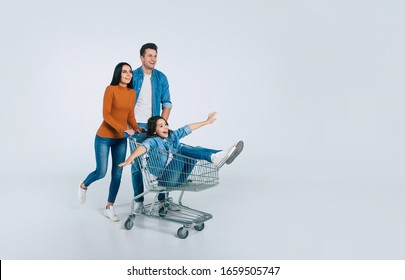 Shopping day. Full-length photo of a young man and his attractive wife, who are laughing, while riding their happy little child in a shopping cart.