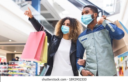 Shopping during quarantine concept. Young african american couple doing shopping together in city mall, wearing protective face masks, panorama. Black lady showing her boyfriend new store, copy space - Powered by Shutterstock