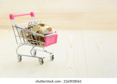 Shopping, E-commerce And Spending Spree Concept : Coins In A Small Pink Shopping Cart Or Trolley On Wood Plank Table. A Shopping Cart, Basket Full Of Nickel, Silver And Bronze Coins In Various Size.