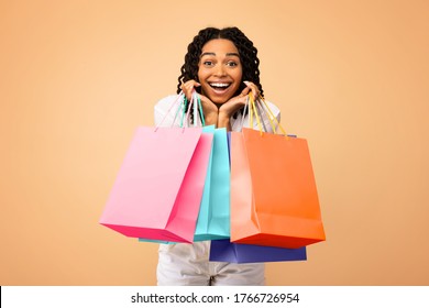 Shopping. Excited African Shopaholic Woman Holding Colorful Shopper Bags On Beige Studio Background, Smiling To Camera