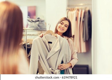 Shopping, Fashion, Clothes, Style And People Concept - Happy Woman Trying Coat On In Mall Or Clothing Store