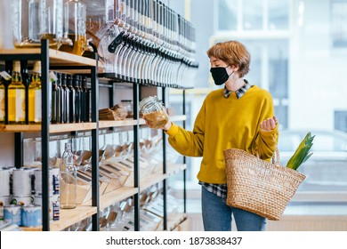 Shopping, Food, Sale, Consumerism Concept. Blond Short Haired Woman In Face Protective Mask Holds Glass Jar With Soya, Buying At Grocery Store Reusable Wicker Basket For Shopping. Zero Waste Concept.