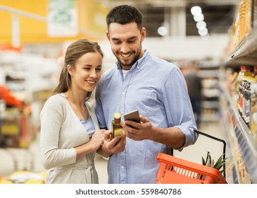 Shopping, Food, Sale, Consumerism And People Concept - Happy Couple With Smartphone Buying Olive Oil At Grocery Store Or Supermarket