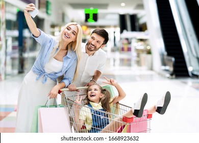 Shopping Fun. Happy Family Taking Selfie On Mobile Phone Riding Little Daughter In Shopping Cart In Mall Center