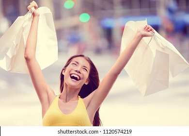 Shopping fun happy girl excited screaming of joy holding shopping bags with arms up in success winning a sale in store. Crazy shopaholic Asian woman spending.