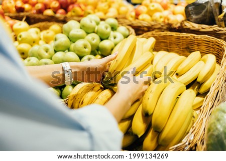 Shopping for groceries, close-up female hands take fresh bananas from store shelf.