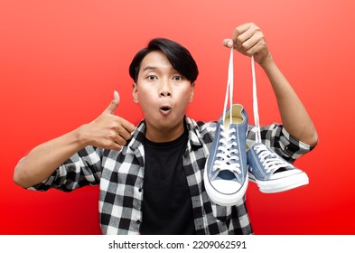 Shopping From Home Concept. A Concept Of Online Shopping Illustrate With Asian Man Holding Phone And Shoes With Happy Expression Isolated Over Red. Man Selling And Buying Stuff In E-commerce