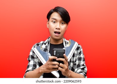 Shopping From Home Concept. A Concept Of Online Shopping Illustrate With Asian Man Holding Phone And Shoes With Happy Expression Isolated Over Red. Man Selling And Buying Stuff In E-commerce