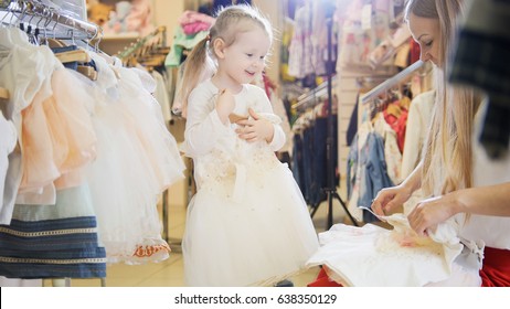 Shopping For Kids - Cute Little Girl With Mommy Buying Dress In Store Of Kids Clothes