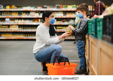 Shopping With Kids During Virus Outbreak. Mother And Child Wearing Surgical Face Mask Buying Fruit In Supermarket. Mom And Little Boy Buy Fresh Vegetable In Grocery Store. Family In Shop.