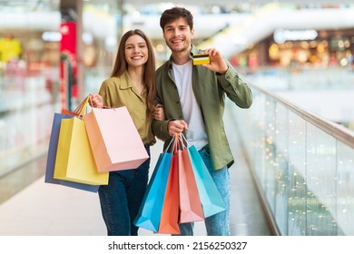 Shopping Offer. Cheerful Couple Showing Credit Card Smiling To Camera Holding Shopper Bags Buying New Clothes And Advertising Great Bank Service In Modern Hypermarket. Commerce Concept - Shutterstock ID 2156250327