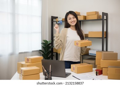 Shopping Online. Young Asian Woman Holding Credit Card For Shopping Payment. Buy Item Online Delivery At Home. Small Business Entrepreneur With Many Parcel Box On Table