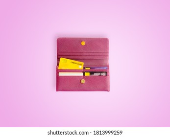 Shopping And Payment Concept From Red Clutch Purse On Pink Background With Credit Cards And Discount Cards In It. Closeup Of Modern Red Leather Wallet. Top View On The Wallet.