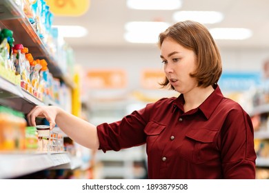 Shopping. Portrait Of A Young Woman Choosing Products Thoughtfully, Reading The Labels On The Packaging. Indoor. The Concept Of Shopping And Conscious Consumerism.