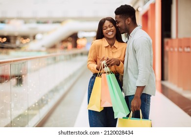 Shopping, Retail, Sales And Discounts. Happy black guy kissing embracing lady, cheerful couple posing holding many bright shopper bags after buying gifts and clothes standing in mall, free copy space