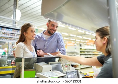 Shopping, Sale, Consumerism, Payment And People Concept - Happy Couple Buying Food At Grocery Store Or Supermarket Cash Register And Cashier Taking Money