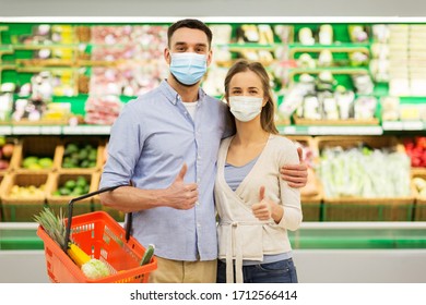 Shopping, Sale, Consumerism And People Concept - Happy Couple Wearing Face Protective Medical Masks For Protection From Virus Disease With Food Basket At Grocery Store Or Supermarket Showing Thumbs Up