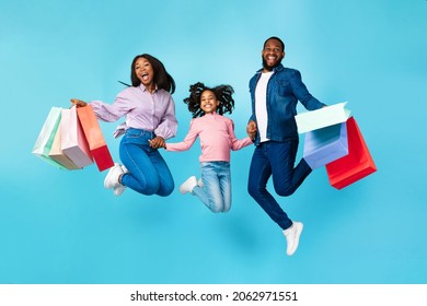 Shopping Together. Happy Family Of Three Excited African American People Jumping Up High In The Air, Holding Hands Carrying Many Bright Shopper Bags Isolated Over Turquoise Studio Background, Advert