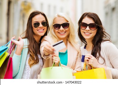 shopping and tourism concept - beautiful girls with shopping bags and credit card in ctiy