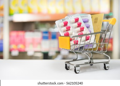 Shopping trolley with blisters of medical capsule pills and credit card with Blurred medicines shelves in pharmacy shop background