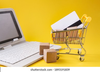 Shopping trolley with boxes, credit card, white laptop on yellow background. Internet Online shopping concept.