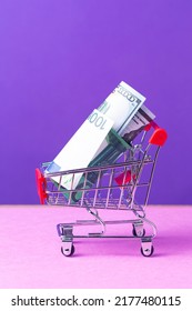 Shopping Trolley Cart With US Dollars And Euro Currency Banknotes Over Trendy Purple Violet Background. Vertical Image