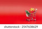 Shopping trolley with Christmas tree and gifts. New Year and Christmas shopping and gift concept. On a red background