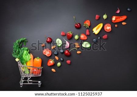 Shopping trolley filled with fresh organic vegetables, fruits and berries on black chalkboard. Top view. Vegetarian, vegan, detox and clean eating concept.
