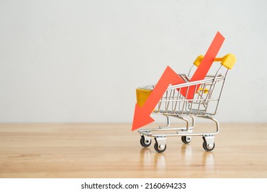 Shopping trolley with red chart falling down on wooden table background copy space. Economic recession crisis, core retail sales decrease, inflation, goods price up, food shortage concept.