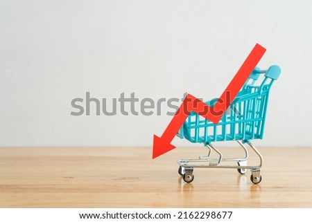 Shopping trolley with red chart falling down on wooden table background copy space. Economic recession crisis, core retail sales decrease, inflation or goods price up, food shortage concept.