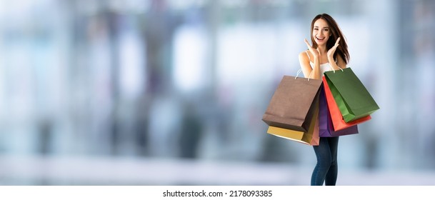 Shopping woman. Happy excited girl, holding many bags, blurred interior or mall background. Copy space area for slogan or sign text. Consumerism and sales ad concept. Wide banner composition image