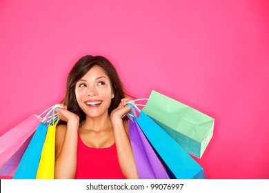 Shopping woman holding shopping bags looking up to the side on pink background at copy space. Beautiful young mixed race Caucasian / Chinese Asian shopper smiling happy.