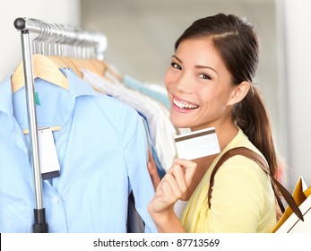 Shopping Woman Showing Credit Card Or Gift Card By Clothes Rack. Happy Smiling Mixed Race Caucasian / Asian Female Shopping In Store.