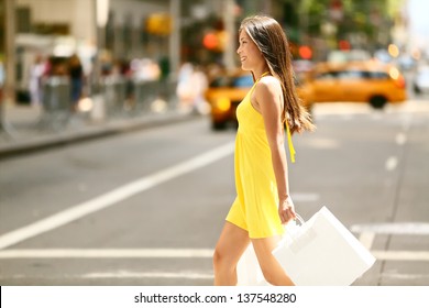 Shopping woman walking outside in New York City holding shopping bags. Shopper smiling happy crossing the street outdoors while on travel on Manhattan, United States. Beautiful model in summer dress.