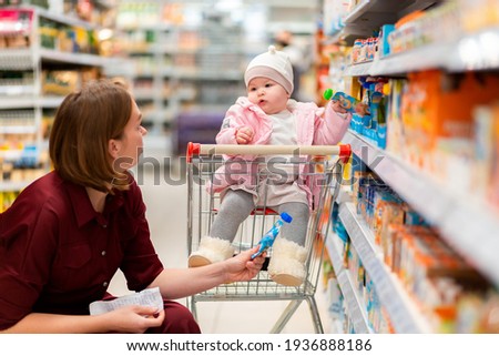 Shopping. A young mother chooses baby food with her baby sitting in a grocery cart. Close up. The concept of family shopping.