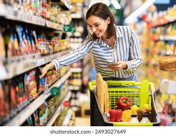 Shopping. Young Smiling Woman Holding And Using Mobile Phone Buying Food Groceries Standing In Supermarket. Female Customer With Smartphone Taking Healthy Products From Shelf At The Shop - Powered by Shutterstock