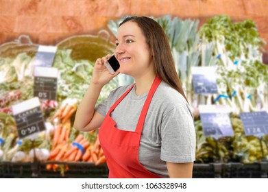 Shopwoman With Apron Using A Smart Phone At The Greengrocer